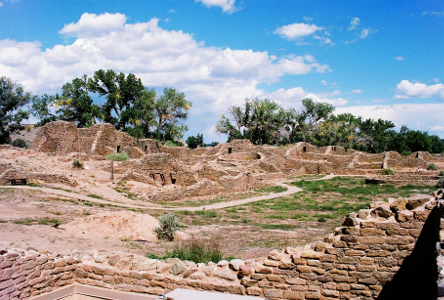 [Partial wall remains are at different heights in different sections of the buildings which seem to be interconnected. While individual bricks are visible, they are 'cemented' together to create walls. There is dirt and grass and a designated path in the center of this section of buildings.]